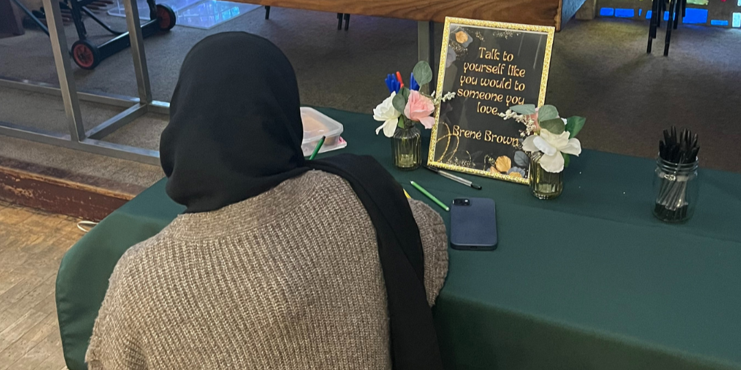 A Muslim woman in a head scarf sits journaling at our wellbeing session